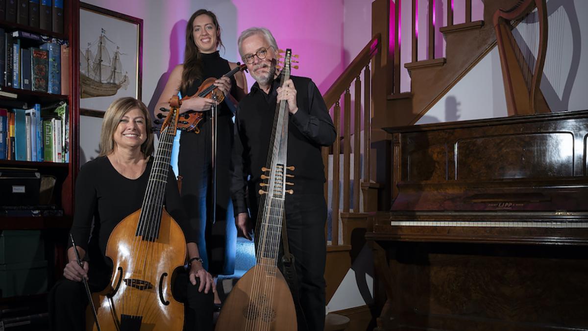 A woman sitting with a vila da gamba, a young woman standing with a violin and man with a beard standing with a theorbo