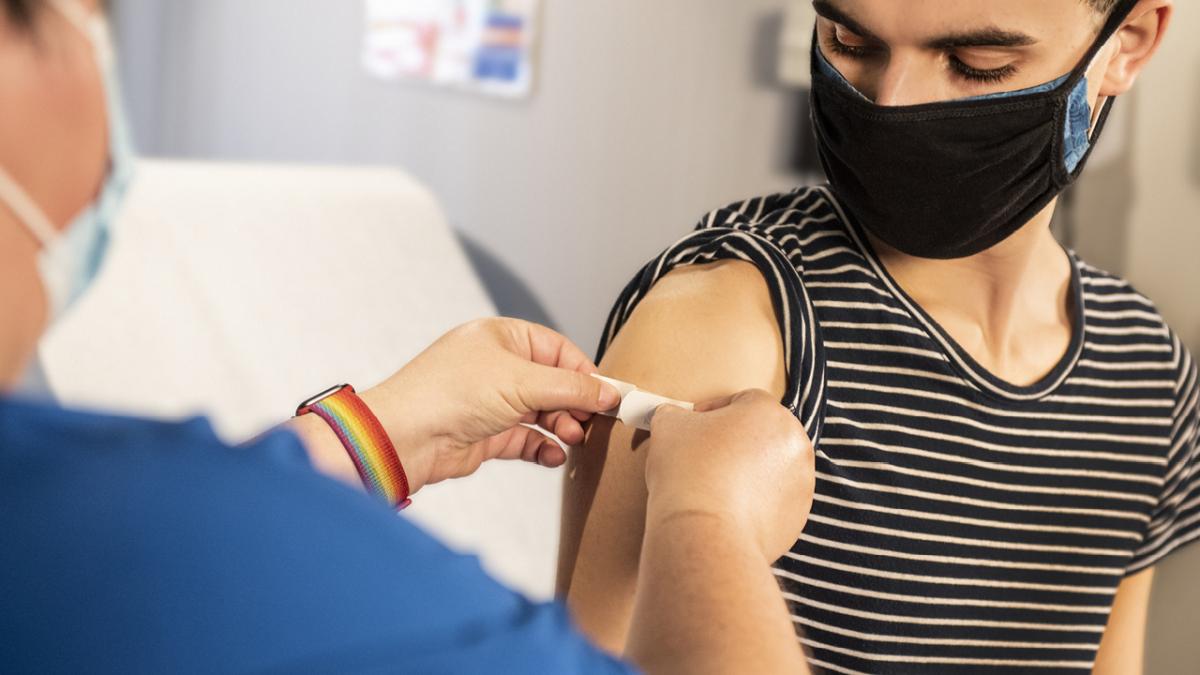 A nurse is putting a bandage on the arm of a man who has received a vaccine